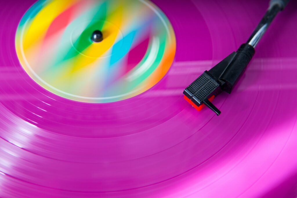 Eine Nahaufnahme einer sich drehenden rosa Schallplatte mit einem bunten Etikett und einer schwarzen Plattenspielernadel.